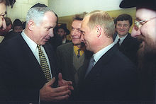 two men, both in their fifties, talking while a crowd of people surround them smiling; one of the two (netanyahu) gestures intently