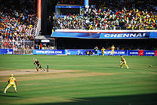 cricketers in a game in front of nearly-full stands.