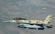  two fighter jets with earth colored camouflage. the squadron emblem, a star of david, and a design resembling a bird of prey are featured on the tail of one aircraft.