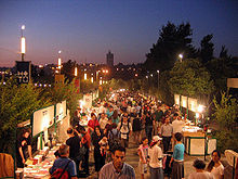 an outdoor book fair at dusk. vendors are in booths along both sides of a walkway crowded with people.